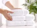 Manos arreglando toallas blancas y esponjosas. Aprende como quitar el olor a humedad de las toallas para que huelan siempre frescas.