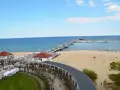 Sopot beach z molo, kawiarniami i spacerującymi ludźmi. W oddali widać statki.