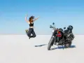 Donna salta di gioia su un deserto di sale, moto pronta per l'avventura. Questo è cosa significa on the road: libertà e scoperta.