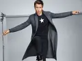 Joven con abrigo largo gris, camiseta negra con estrella blanca y vaqueros oscuros. Explora diversos tipos de abrigos para tu estilo.