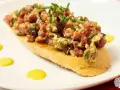 Tosta con steak tartar de salchichón y cebollino picado, decorada con puntos de salsa amarilla.