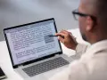 Un homme examine un document sur un écran d'ordinateur, soulignant des passages pour apprendre comment reconnaître une pièce fautée.
