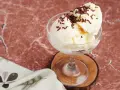 Cremiges Litschi Eis mit Schokostreuseln in einem Glas auf einem Holzuntersetzer.