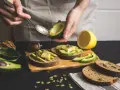 Preparazione di gustose ricette con avocado: toast con avocado, formaggio e semi.