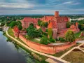 Malbork, największy zamek w Polsce, majestatycznie wznosi się nad rzeką Nogat. Czerwona cegła i strzeliste wieże tworzą imponujący widok.