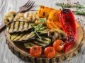 Grillowane warzywa: bakłażan, papryka, pieczarki, pomidorki i marchewka. Idealne dodatki do grilla, podane na drewnianej desce.