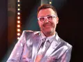 DJ Adamus w srebrnym garniturze i białych okularach, uśmiecha się. Czy to jego odpowiedź na pytanie "Jaka to melodia?