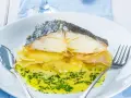 Pescado al horno con patatas y cebolla, bañado en aceite de oliva y perejil. Un plato delicioso y reconfortante.