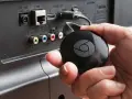 En hand håller en svart Chromecast för att ansluta till en HDMI-port på baksidan av en TV.