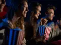 Uśmiechnięci ludzie jedzą popcorn w kinie. Idealny strój do kina to coś wygodnego, jak na przykład bluza.