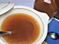 Caldo de carne casero en una cazuela blanca con tapa, junto a una jarra y cucharas.