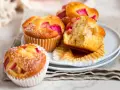 Saftige Rhabarber Muffins, mit Puderzucker bestäubt, auf einem Teller gestapelt. Einer ist angeschnitten und zeigt die rosa Rhabarberstücke.
