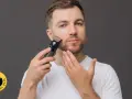 Hombre con barba usando una recortadora para perfilar su rostro. El accesorio "Testado por el país" aparece en la esquina inferior izquierda.