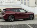 Ciemnoczerwone BMW iX stoi na brukowanym podjeździe przed eleganckim budynkiem.