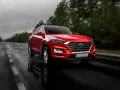 Czerwony Hyundai Tucson jedzie po mokrej drodze w deszczowy dzień. Warto pamiętać o filtrze CPL, którego zastosowanie poprawia widoczność w takich warunkach.