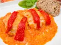 Bacalao a la riojana, un plato tradicional con trozos de pescado blanco cubiertos de pimientos rojos y una salsa de tomate y pimientos. Servido con pan y hojas verdes.