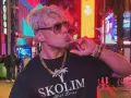 Skolim w okularach i złotych łańcuchach, pozuje na tle neonów. Król Latino w swoim wieku, w blasku miasta.