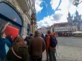 A group of tourists on a prague free walking tour gather on a cobblestone street, with historic buildings and a church in the background.