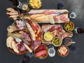 Eine reichhaltige Wurstplatte anrichten mit Baguette, Oliven, Cornichons und Senf.