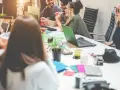 Grupa młodych ludzi, pokolenie gen y, pracuje razem przy biurku, śmiejąc się i dyskutując.
