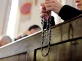 Dłonie trzymające różaniec podczas nabożeństwa. W tle widać innych wiernych, przygotowujących się na odpust.
