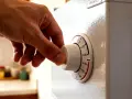 Dłoń kręci pokrętłem termostatu lodówki, ustawiając temperaturę.
