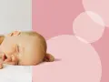 Śpiący, 2 tygodniowy noworodek otulony białym kocykiem. Delikatne różowe tło z okręgami.