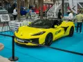 Jaskrawożółty Chevrolet Corvette C8 z czarnym dachem i felgami, prezentowany na niebieskiej podłodze wystawowej.