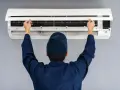 Tecnico con cappellino blu apre il pannello di un climatizzatore per impostare aria fredda.