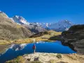 Randonneur contemplant un lac alpin aux reflets parfaits, un paysage grandiose qui pourrait faire partie d'un GR5 itinéraire complet.