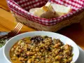 Un reconfortante cocido montañés, con garbanzos, verduras y trozos de carne, servido en un cuenco blanco. A su lado, una cesta con pan y un tenedor.
