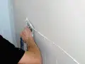 Ręka nakłada gładź na ścianę, tworząc idealnie prostą linię. To precyzyjne sztablatura dla malarza.