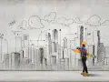 Młoda kobieta w kasku, z wielkim ołówkiem, rysuje na ścianie szkic miasta. Czy architektura jest trudna? To zależy od perspektywy!