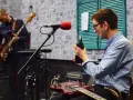 Dwóch muzyków w studiu nagraniowym. Jeden gra na basie, drugi trzyma słuchawki, gotowy do nagrania. Słychać początek melodii.
