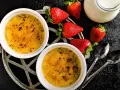 Zwei cremige Crème brûlée mit karamellisierter Kruste, garniert mit frischen Erdbeeren und einem Milchkännchen.
