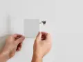 Hands apply a mesh patch to a hole in a white wall, demonstrating how to patch a hole in the wall.