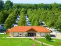 Słoneczny dzień na kempingu Liptot. Ludzie odpoczywają na trawie, a w tle widać rzędy kamperów i przyczep kempingowych wśród drzew.