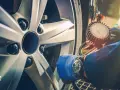 Controllo pneumatici con manometro su cerchio Ford. Guanto blu e orologio da polso.