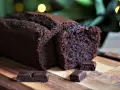 Un délicieux cake au chocolat, moelleux et intense, coupé en tranches sur une planche en bois, avec des carrés de chocolat noir en garniture.