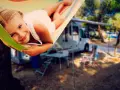 Ein glückliches Mädchen entspannt sich in einer Hängematte auf einem familienfreundlichen Campingplatz. Im Hintergrund stehen Wohnmobile und Campingmöbel.