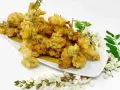 Fiori di acacia fritti, dorati e croccanti, serviti su un piatto bianco con rametti di fiori e foglie fresche.