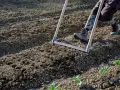 Persona che lavora il terreno con un rastrello, preparando l'orto per la semina.
