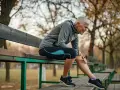 Kvinna med benhinneinflammation utsida sitter på en bänk och håller sig om smärtande underbenet.