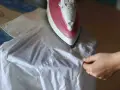 Dłoń układa białą koszulę na desce do prasowania. Gorące żelazko zaraz wygładzi materiał, a pytanie brzmi: czy rękawy koszuli prasuje się na kant?