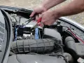 Ręce podłączają kable do akumulatora, bo auto nie odpala.