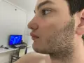 Perfil de un joven con barba incipiente, preparándose para afeitar barba. Al fondo, un monitor con pantalla azul.