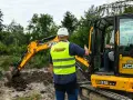 Szkolenie na koparkę w Akademii Operatora. Instruktor w kamizelce odblaskowej pokazuje, jak uzyskać uprawnienia na koparkę.