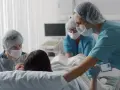 W szpitalu rodząca kobieta, wspierana przez partnera i pielęgniarkę. Czas porodu jest kluczowy.