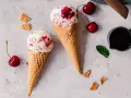 Zwei Waffelhörnchen mit Joghurt Kirsch Eis, garniert mit frischen Kirschen und Minze.