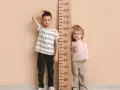 Chłopiec i dziewczynka mierzą wzrost przy drewnianej miarce. Chłopiec ma około 104 cm, co odpowiada wiekowi 4 lat.
